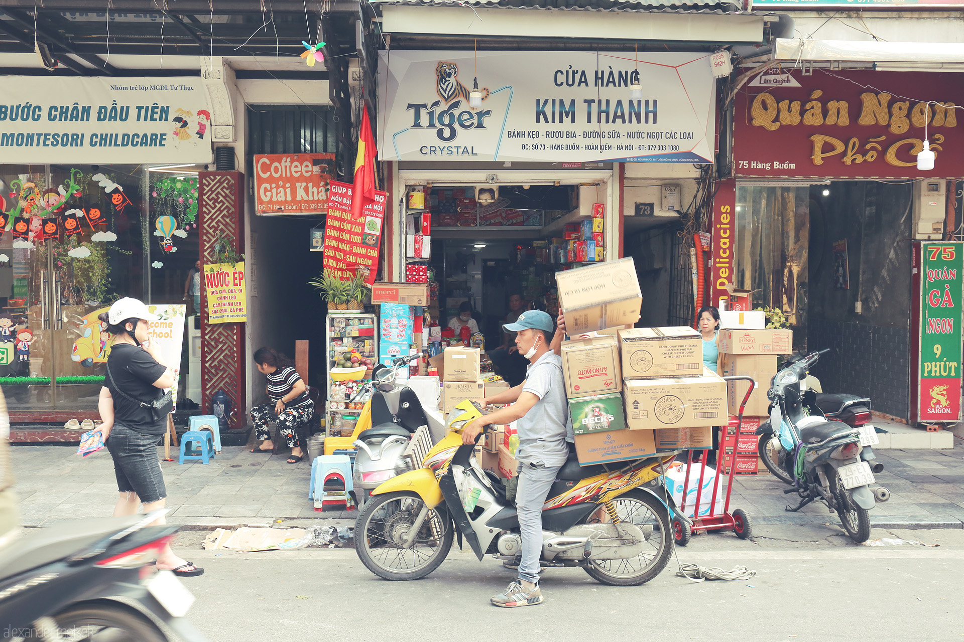 Foto von A deliveryman balances boxes on a motorbike, weaving through the vibrant bustle of Hàng Buom, Hanoi’s iconic street life.