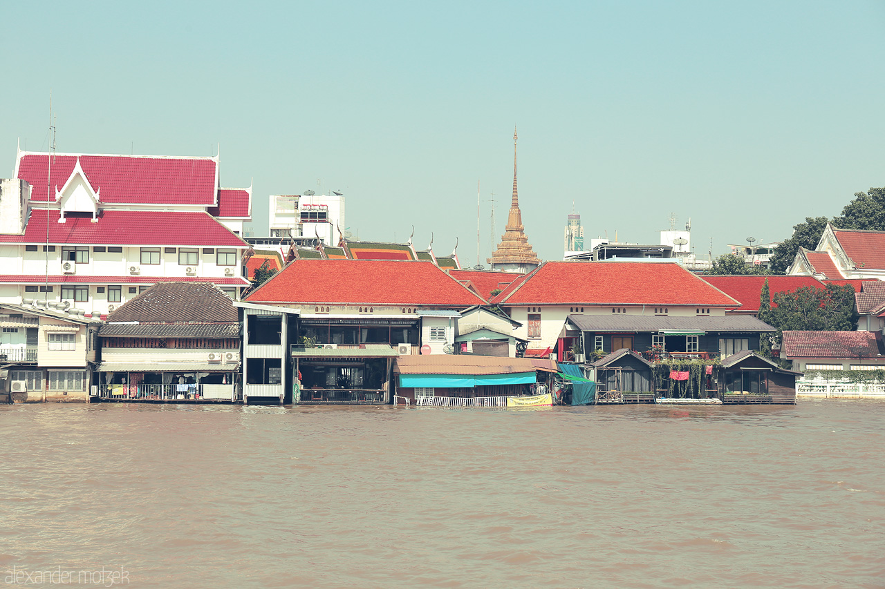 Foto von Tranquil views of vibrant red-roofed homes along the Chao Phraya River in Khlong San, Bangkok, with a distant temple spire.