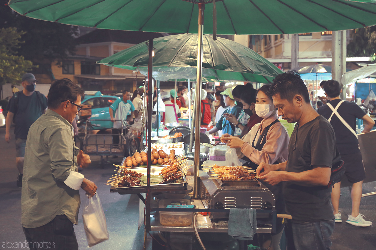 Foto von Vibrant street food scene at Talat Yot, Bangkok. Locals delight in skewers and snacks under the glow of green umbrellas.