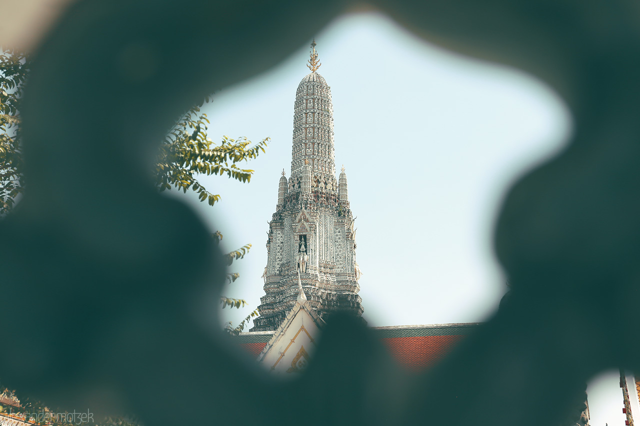 Foto von Wat Arun's spire, framed through ornate lattice, stands tall by the Chao Phraya River, Bangkok, capturing serene elegance and architectural beauty.