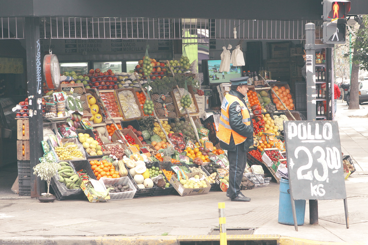 Foto von A vibrant street market in Buenos Aires showcases colorful fruits and vegetables under the watchful eye of a traffic officer. Everyday life unfolds.