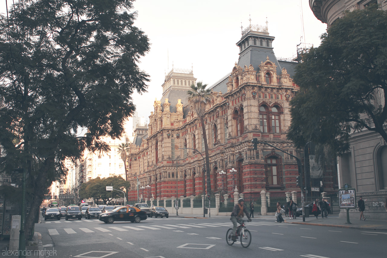 Foto von Cyclist breezes past the ornate Palacio de Aguas Corrientes in Buenos Aires, capturing urban elegance.