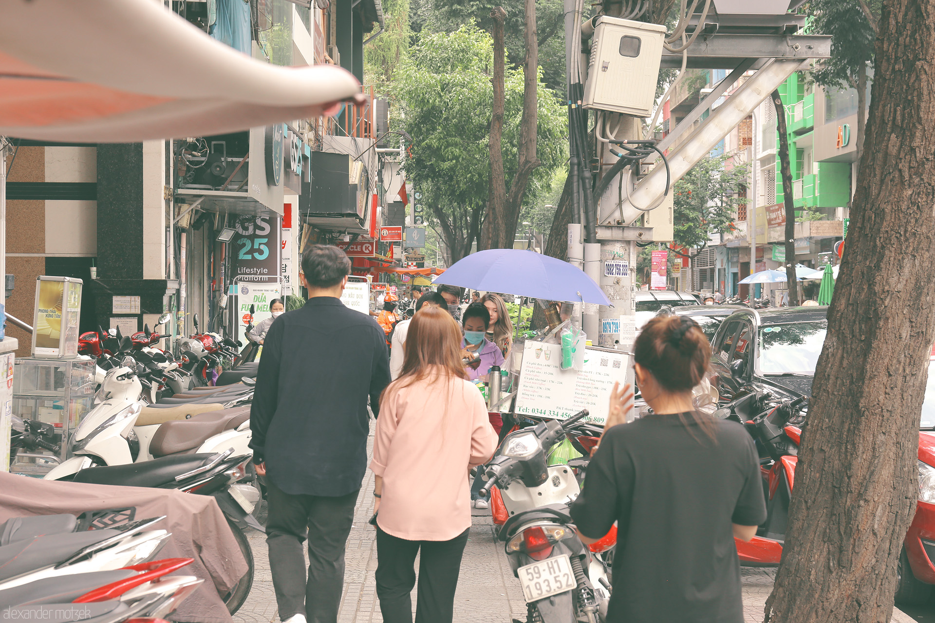 Foto von Bustling Saigon sidewalk: motorbikes, street vendors, and city life under umbrellas in Ho Chi Minh City, Vietnam.