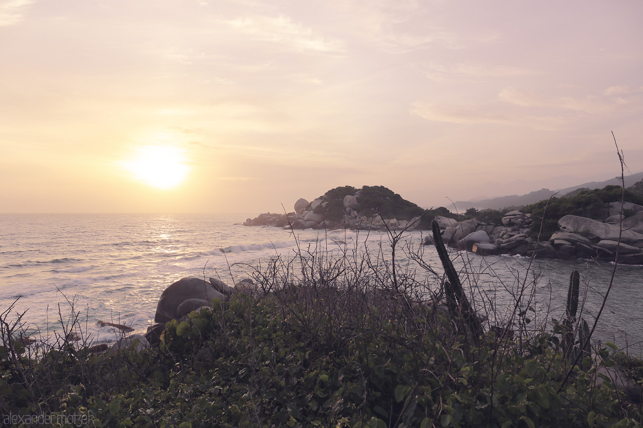 Foto von A sublime sunrise illuminates the rugged coast of Tayrona, Santa Marta, Colombia with hues of lavender and gold, evoking a serene and untouched paradise.