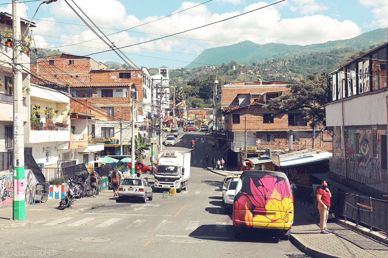 Foto von A vibrant, bustling street in Comuna 13, Medellín, lined with colorful street art and vibrant activity against a backdrop of distant mountains.