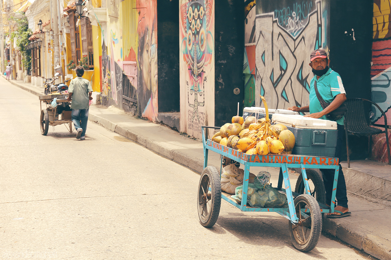 Foto von A vibrant street scene in Cartagena, Colombia featuring a local vendor selling coconuts and a colorful mural backdrop.