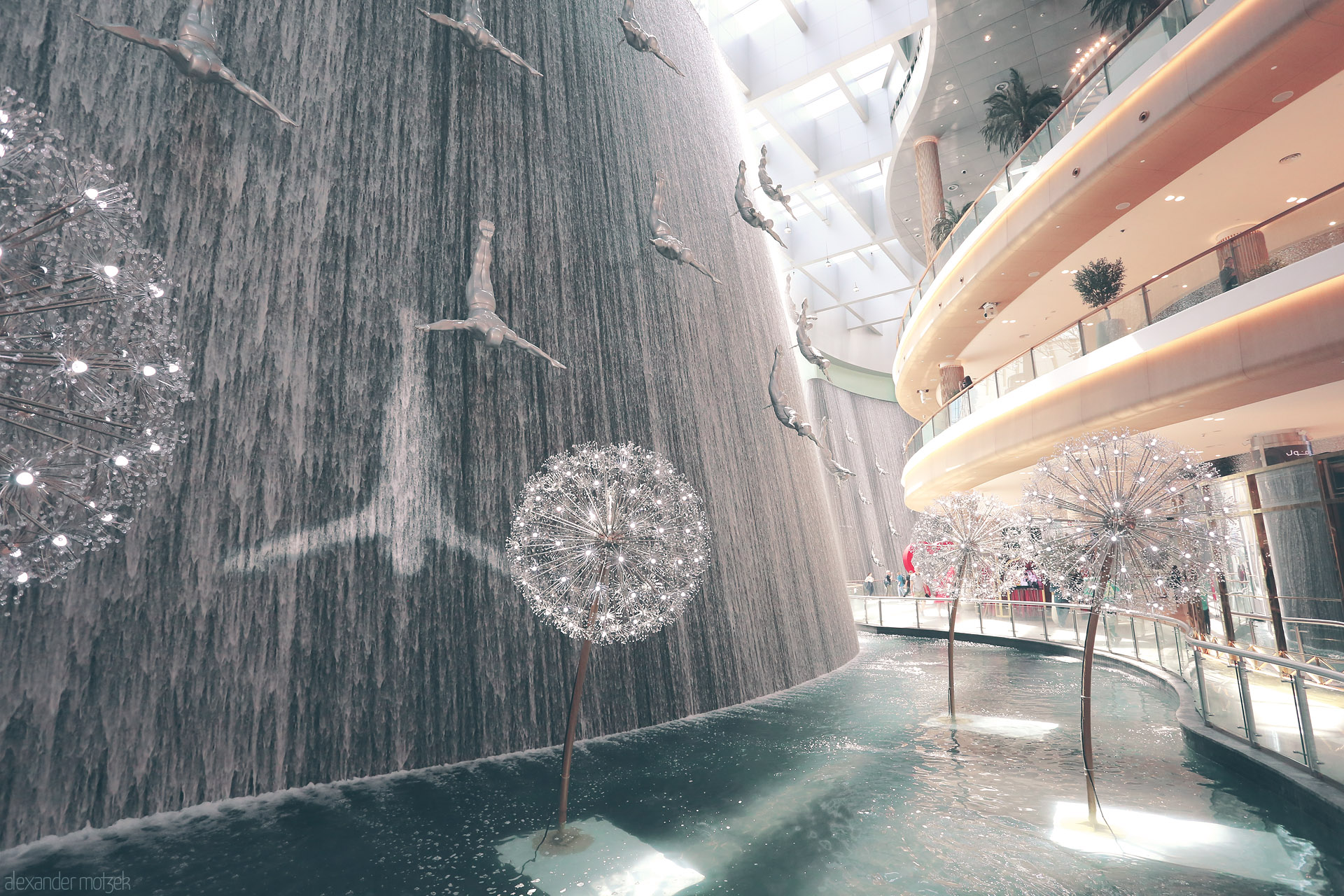 Sama Soaring: Dubai Drifters Foto von Divers soar through a cascading waterfall inside Dubai Mall, where art and water meet under the light of modern dandelions.