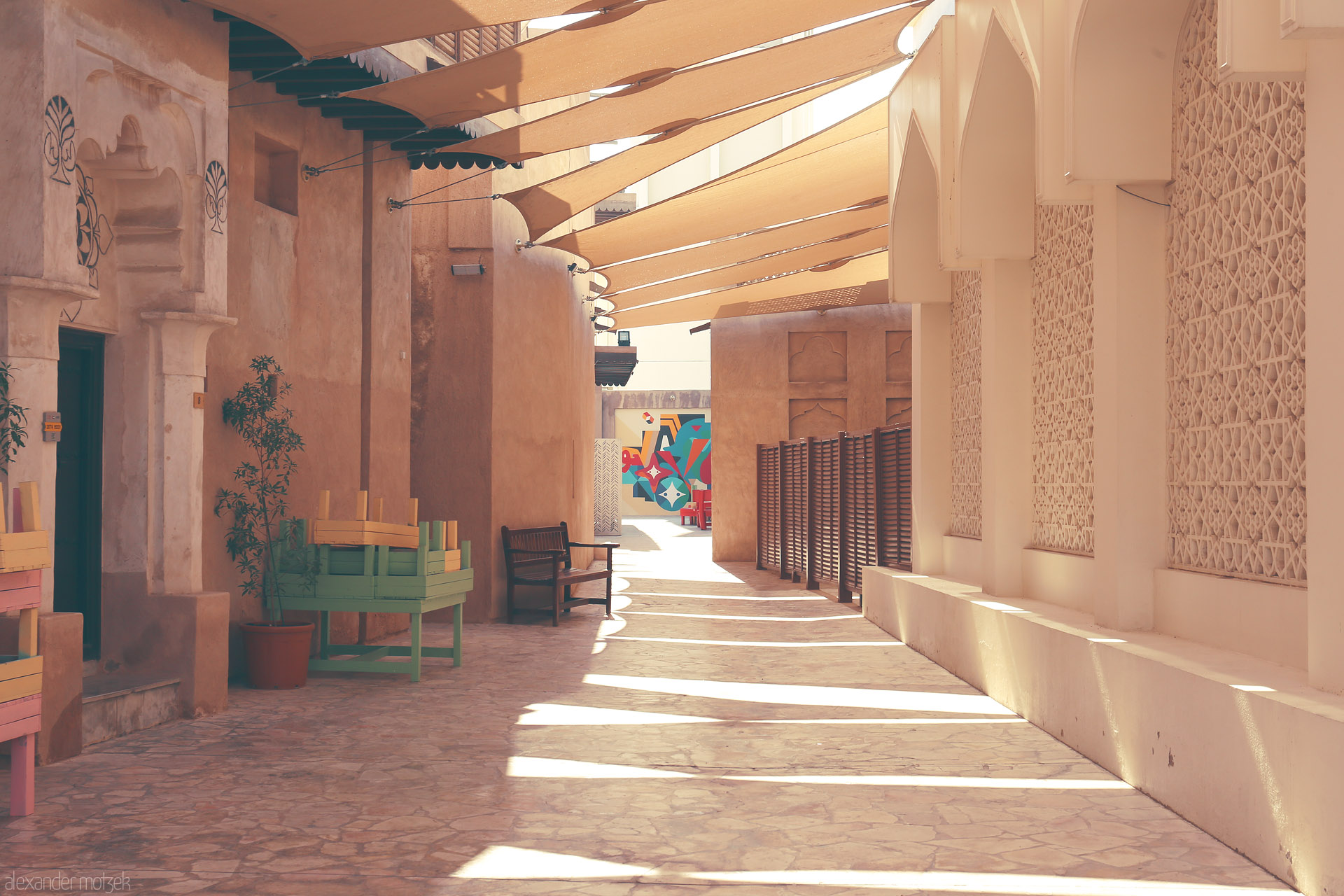 Foto von Golden rays dance on heritage walls and pastel benches in a quiet Al Seef alley, Dubai, where tradition meets vibrant street art.