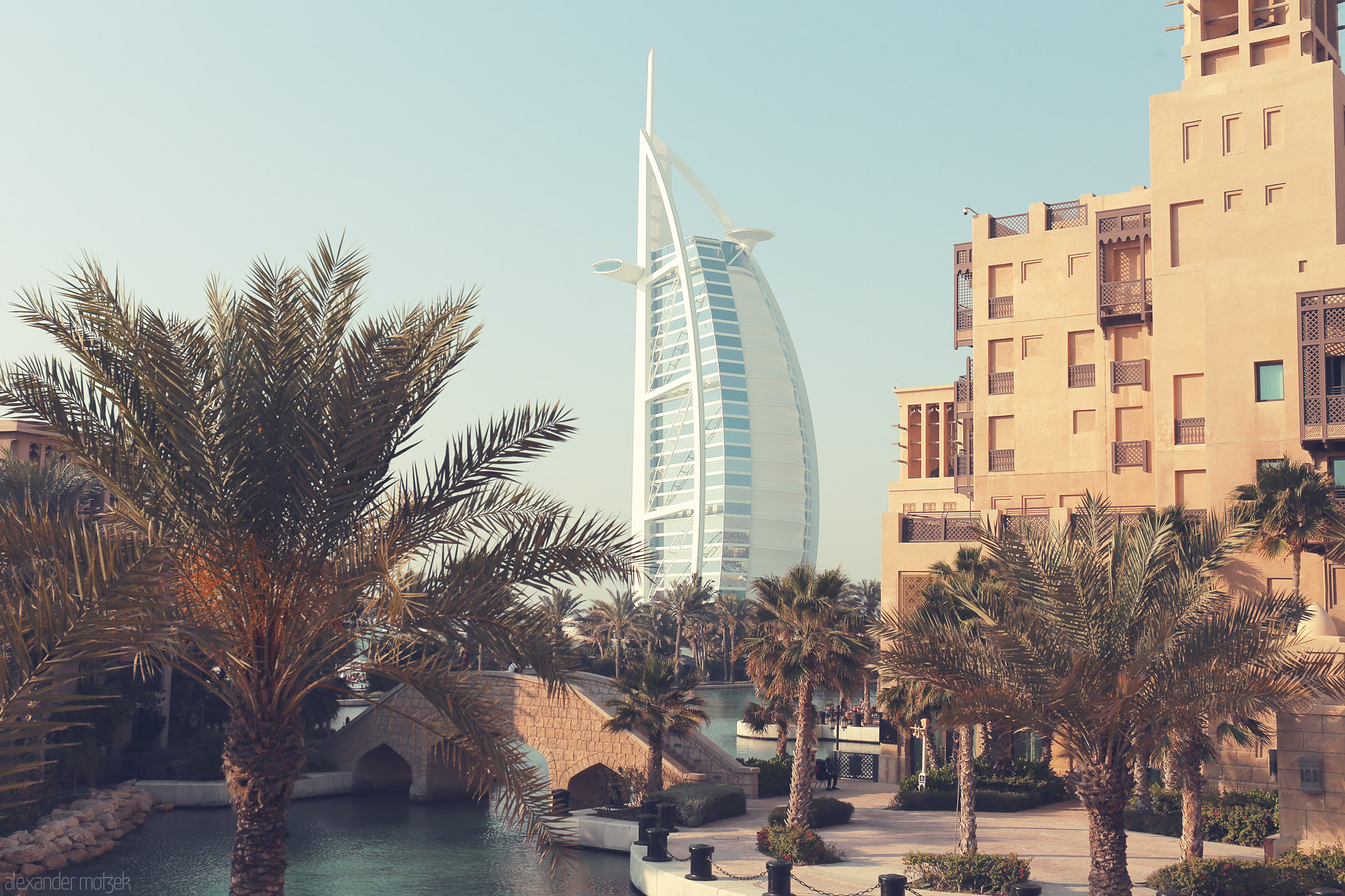 Oasis of Opulence Foto von Palm trees and tranquil water frame the iconic Burj Al Arab in sunlit Dubai, blending tradition and modern luxury on the Arabian Gulf.
