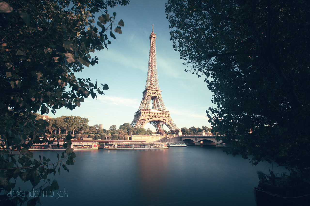 Foto von The Eiffel Tower majestically rises beside the serene waters of the Seine, framed by lush trees on a tranquil Parisian day.