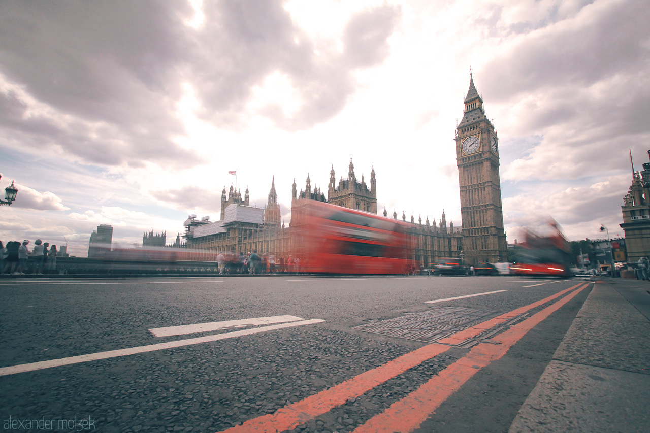 Foto von Big Ben and busy red buses, captured in motion on Westminster Bridge under a cloudy London sky.