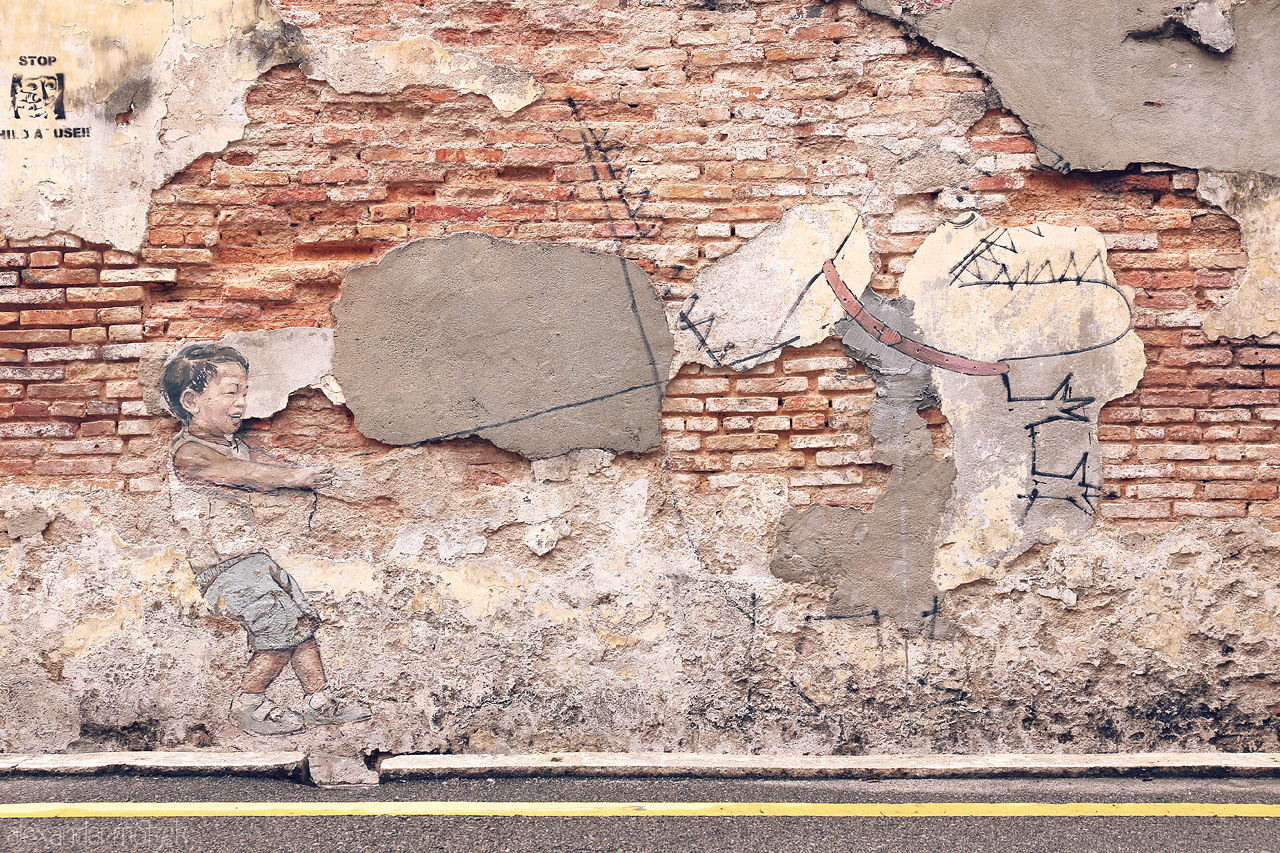 Foto von A playful mural in Penang captures a child pulling on a prehistoric creature. A blend of art and heritage on weathered walls.