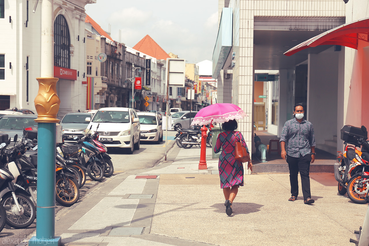 Foto von A vibrant street scene in Penang, Malaysia, featuring a colorful umbrella, lively local architecture, and bustling city life.