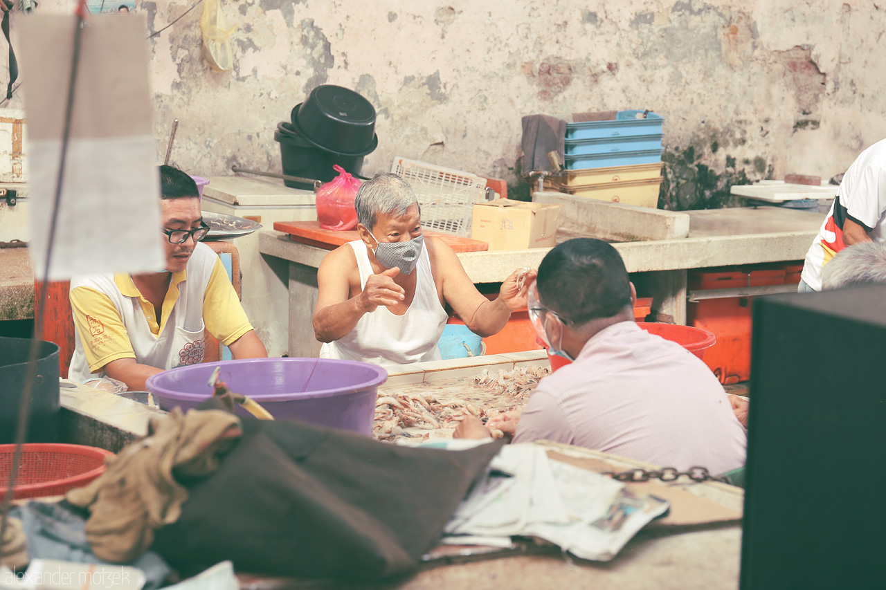 Foto von Locals engage in lively conversation at a bustling street market in Penang, Malaysia, surrounded by fresh produce and vibrant colors.