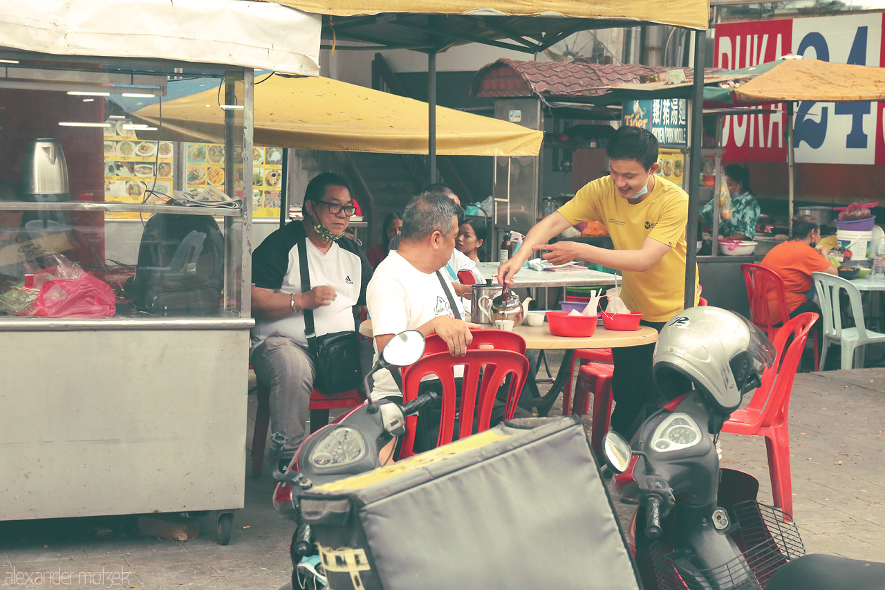 Foto von Locals share laughs over steaming bowls at a bustling Kuala Lumpur street stall, capturing the vibrant spirit of Malaysian street life.