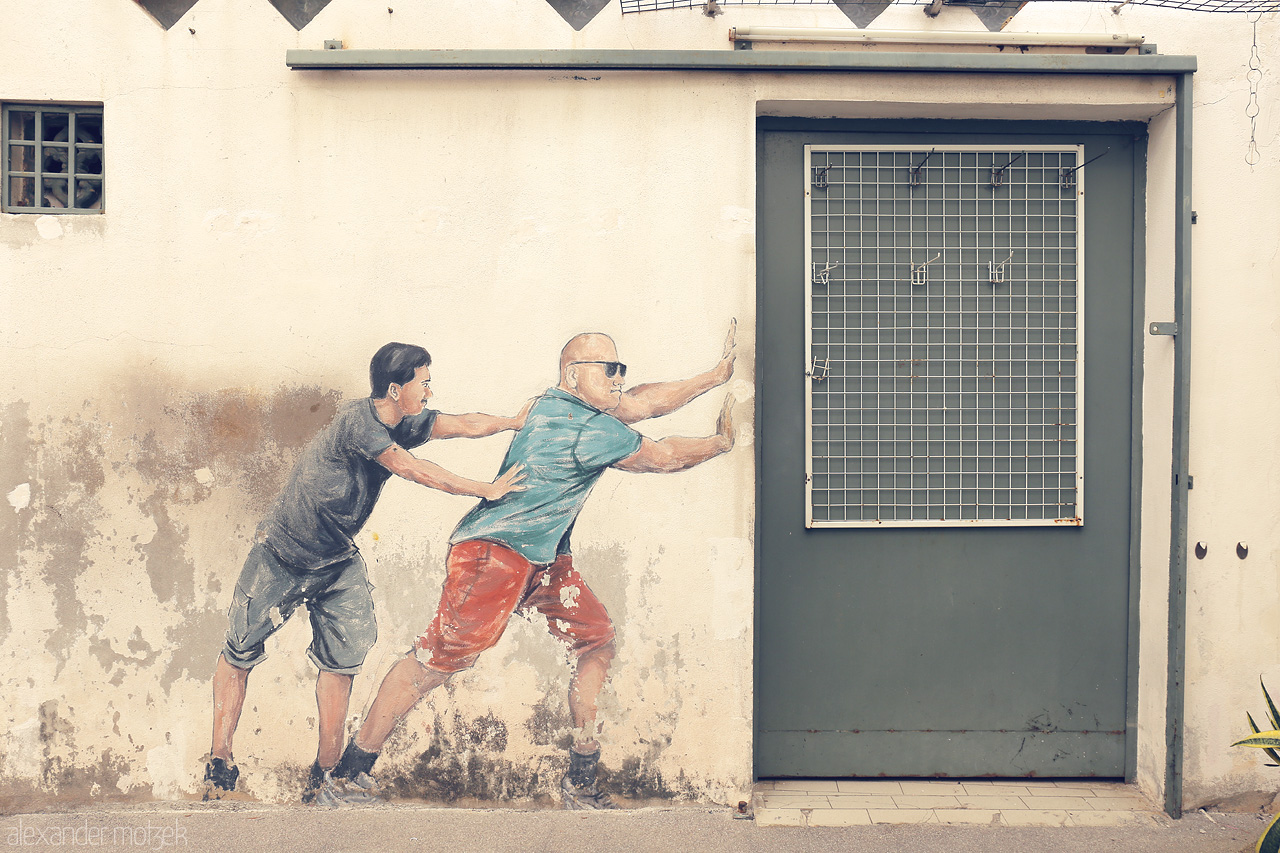 Foto von Street art in Penang, Malaysia, shows two figures pushing an actual door, blending reality with mural artistry in a whimsical urban scene.