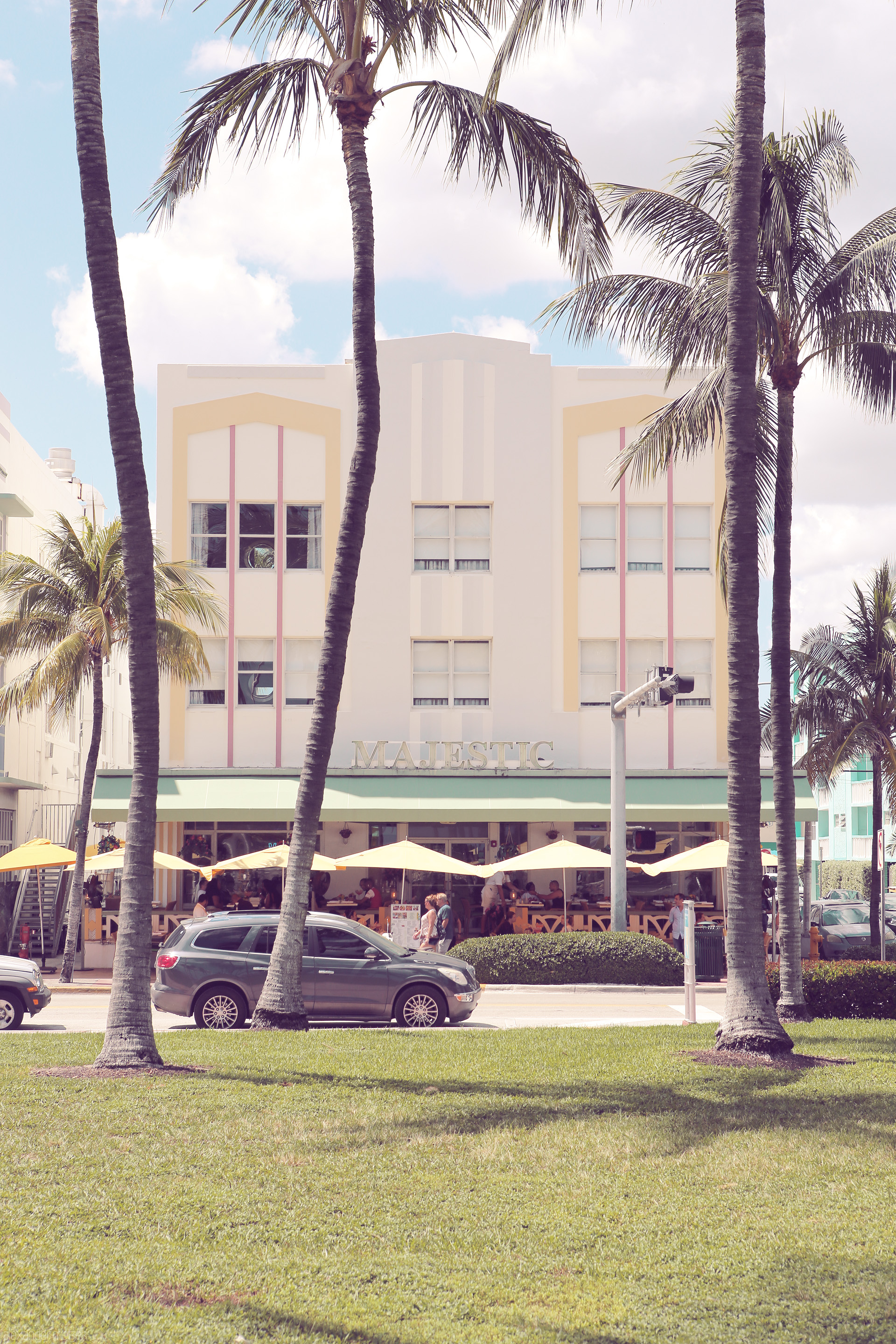 Foto von A pastel Art Deco building on Ocean Drive, Miami, framed by palm trees under a sunny sky.