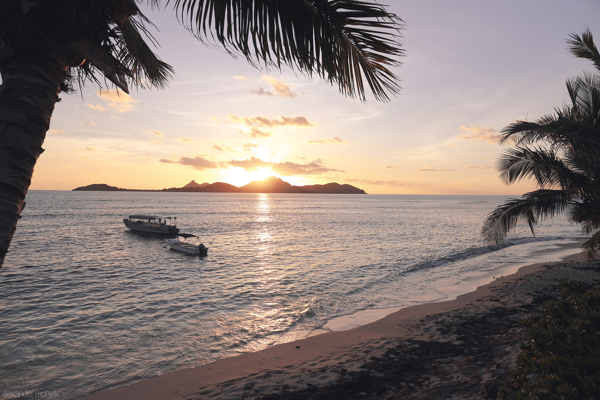 Foto von Palm-framed Tokoriki sunset with two boats on calm water, sandy beach in foreground, and island silhouettes on the horizon, Fiji.