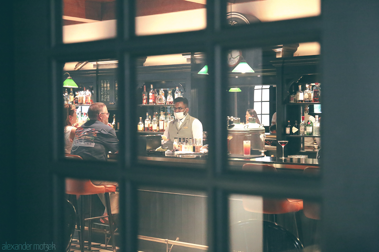 Foto von Raffle's cozy bar in Singapore where locals and travelers share stories over drinks. Captured through a window, the bartenders mix magic in every glass.