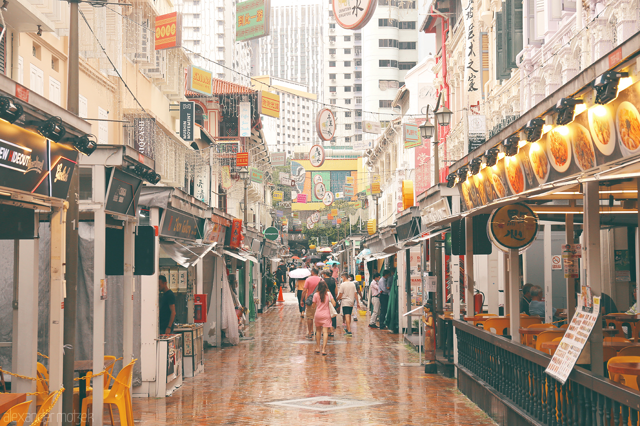 Foto von Travelers stroll through a vibrant, rain-kissed street in Singapore’s Chinatown, soaking in the harmonious blend of modernity and tradition.