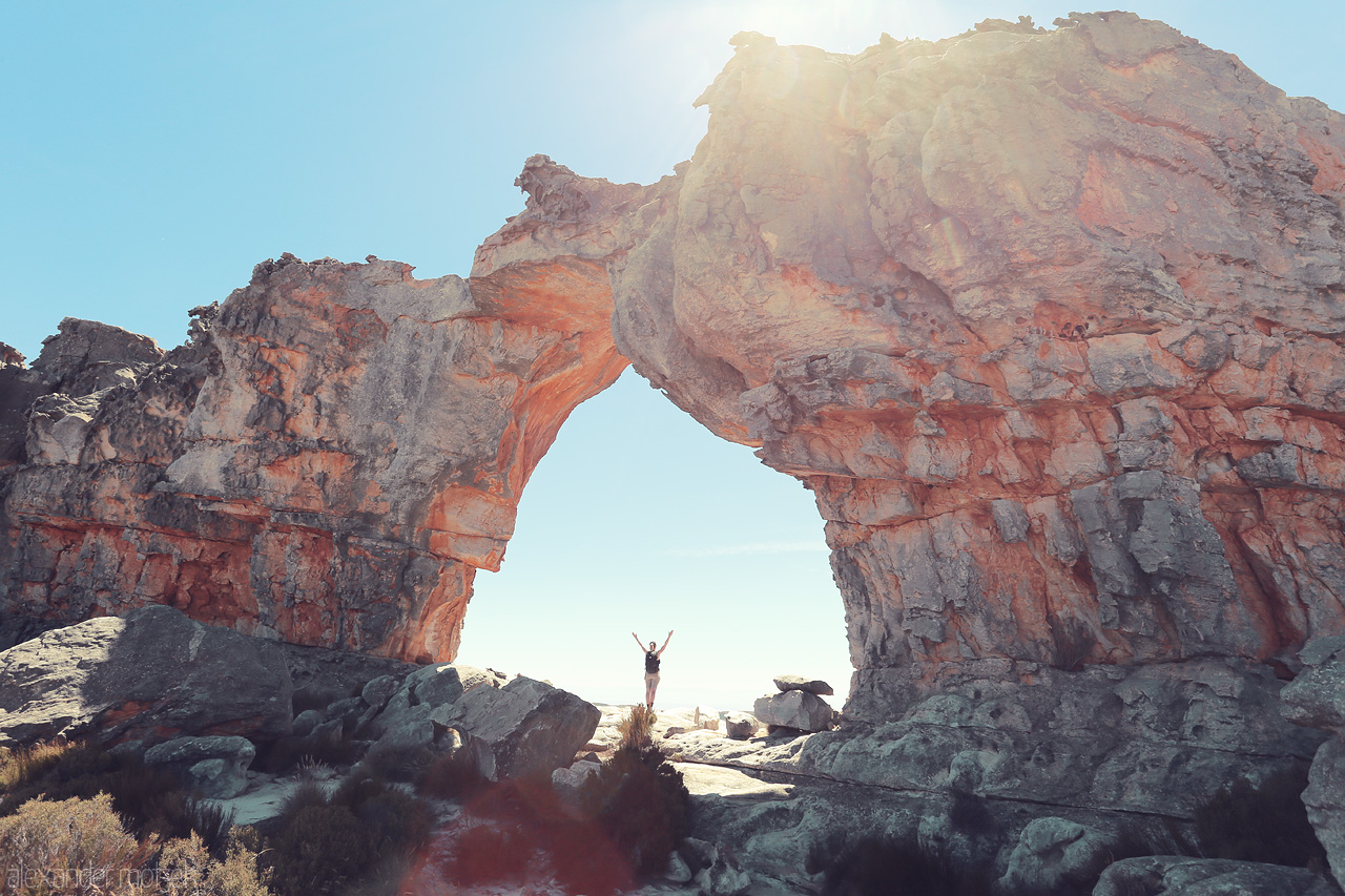 Foto von A lone traveler stands beneath the majestic rock arch in Cederberg, South Africa, basking in sunlight and nature's grandeur.