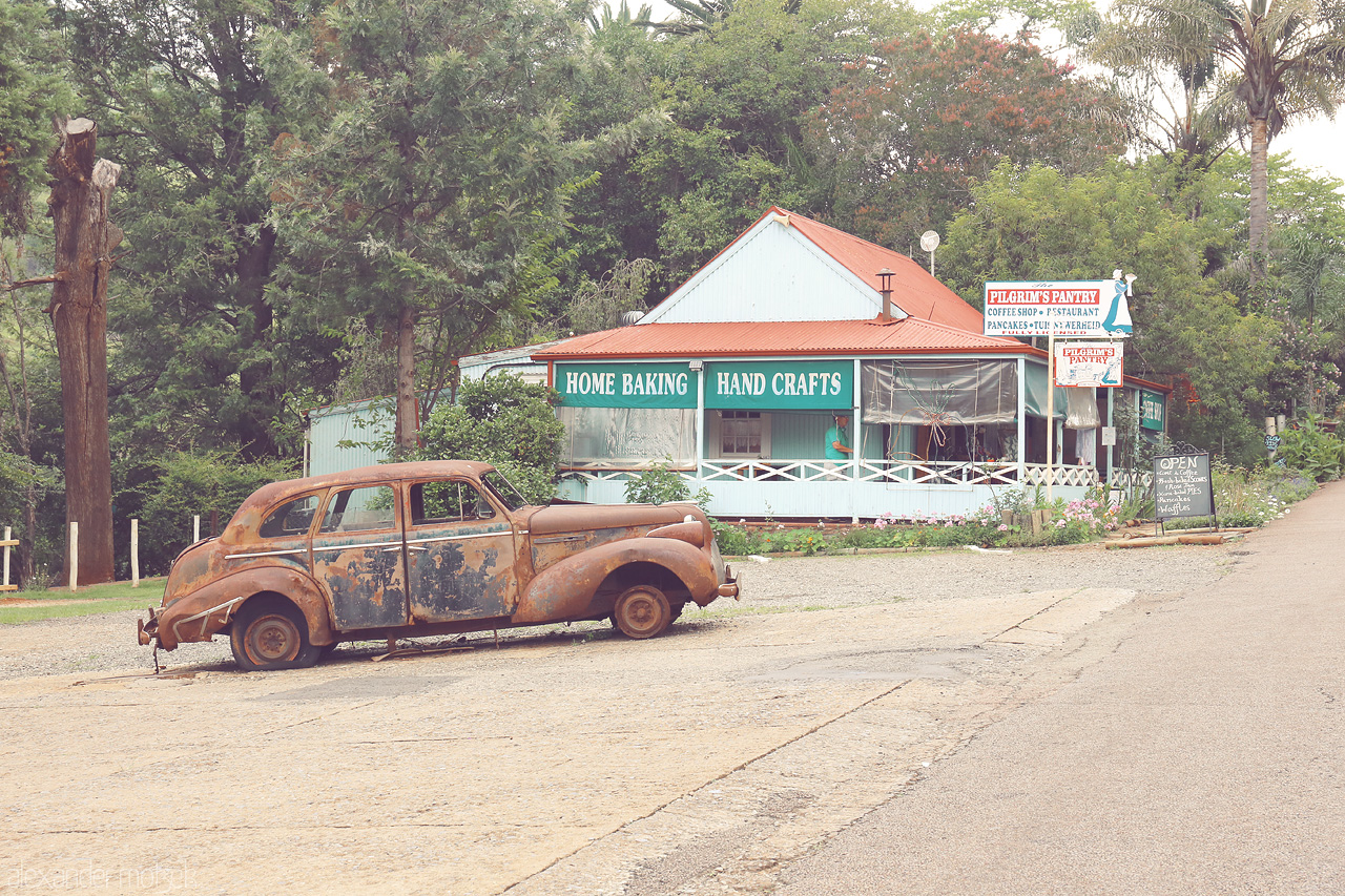 Foto von A rusty car rests peacefully before a quaint handcraft shop in Pilgrim's Rest, South Africa.