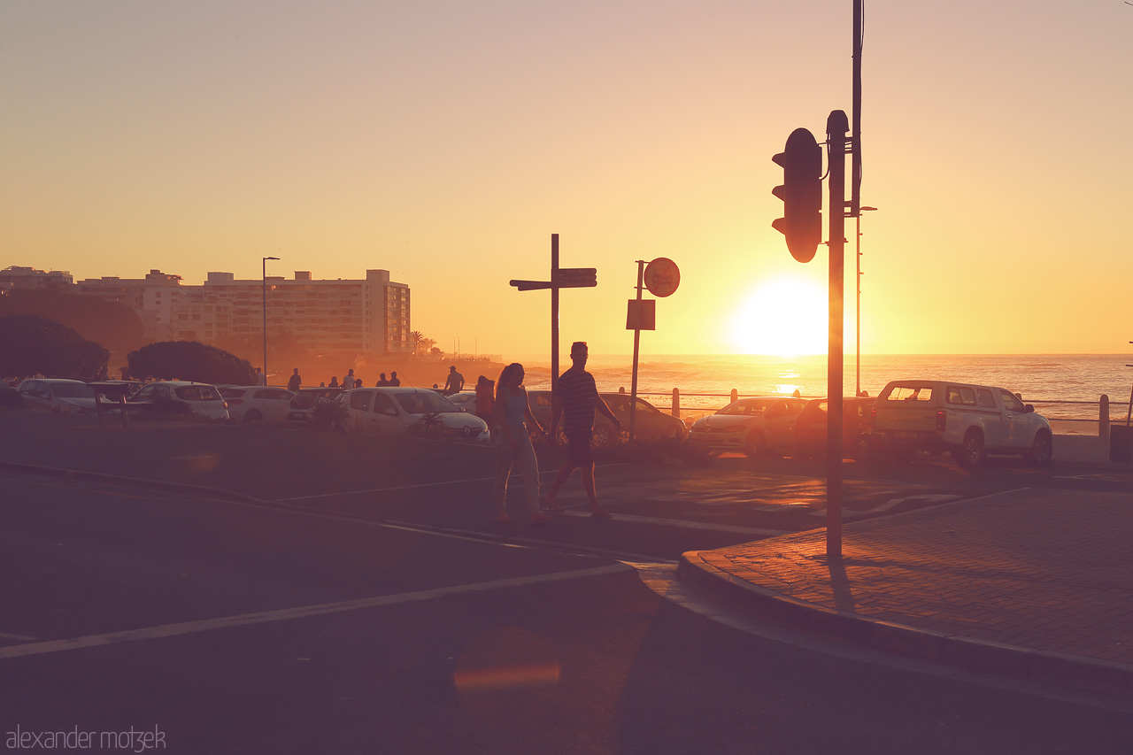 Foto von Couple strolls at sunset in Cape Town, with silhouettes against the ocean's golden horizon.