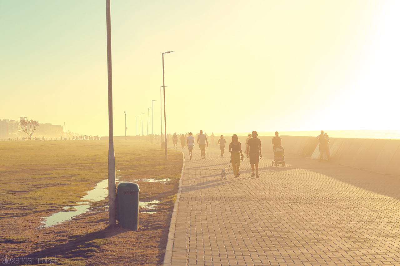 Foto von Silhouetted figures walk along Cape Town's sun-drenched seafront promenade in a golden haze.