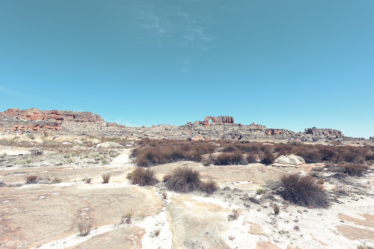 Foto von Sunlit rock formations and hardy shrubs under a vast sky in Cederberg, South Africa. A stark yet stunning natural tapestry.