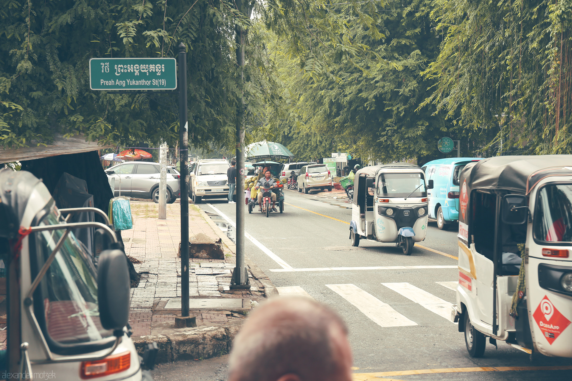Foto von Tuk-tuks weave through leafy Preah Ang Yukanthor St in vibrant Phnom Penh, capturing Cambodia's street life energy.