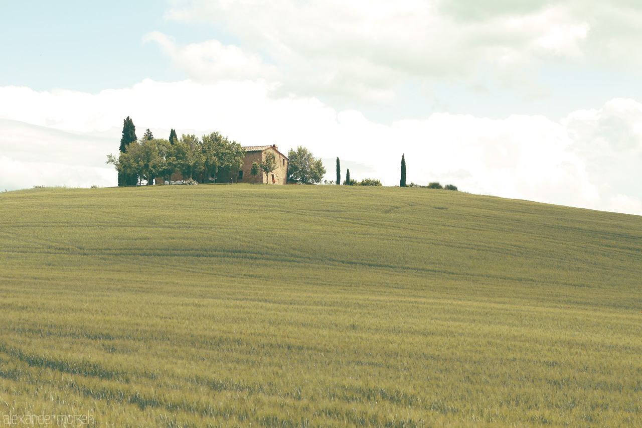 Foto von Rolling Tuscan hills embrace a solitary farmhouse under a sky of gentle clouds.