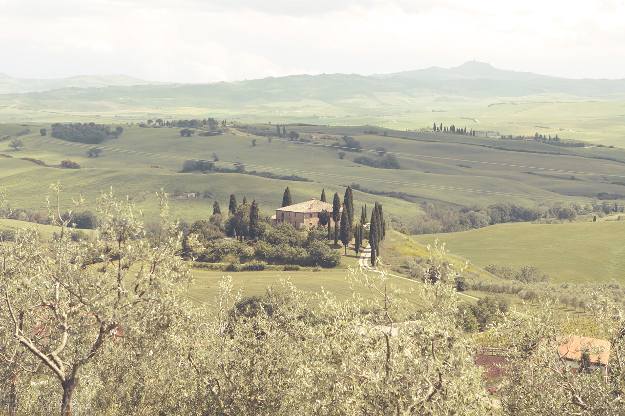 Foto von Rolling hills of Tuscany embrace a secluded villa, framed by iconic cypress trees under an expansive sky.