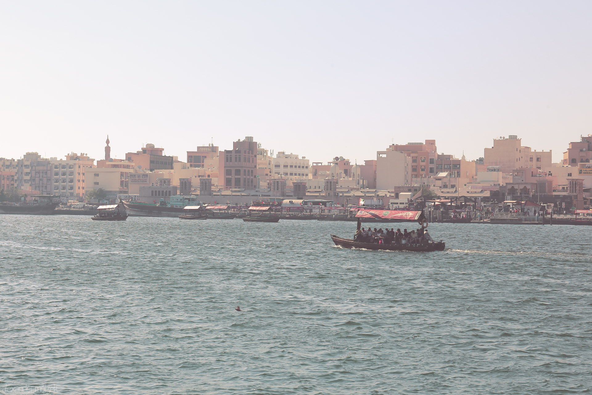 Foto von Traditional abra ferries glide across Dubai Creek, framed by old Deira’s pastel skyline and the subtle haze of an Emirati afternoon.