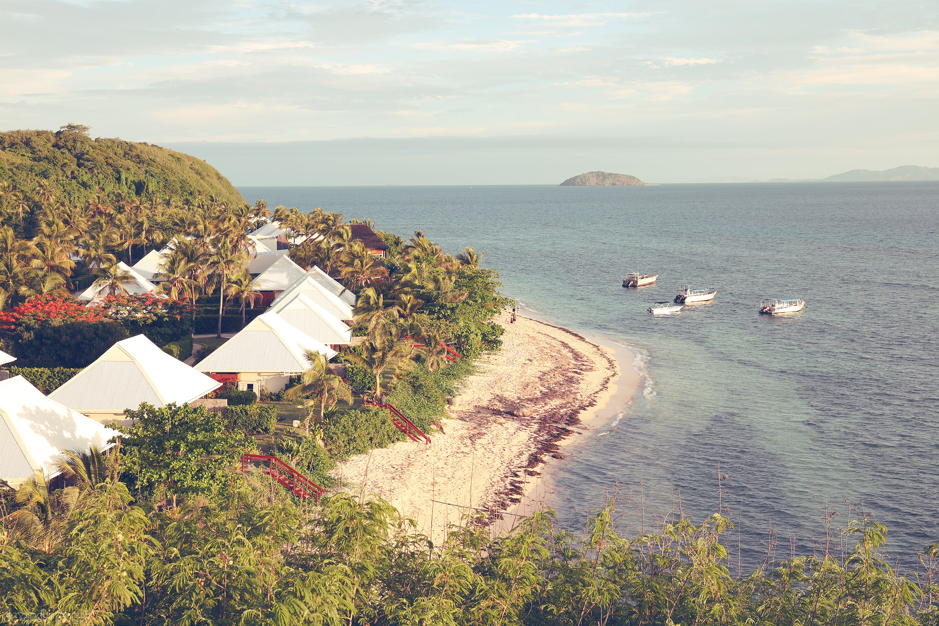 Foto von White-roof villas and palms curve along a sandy shore in Tokoriki, Fiji, with small boats floating on the calm Mamanuca sea.